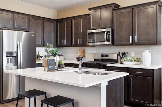 kitchen featuring stainless steel appliances, dark brown cabinets, an island with sink, and light countertops