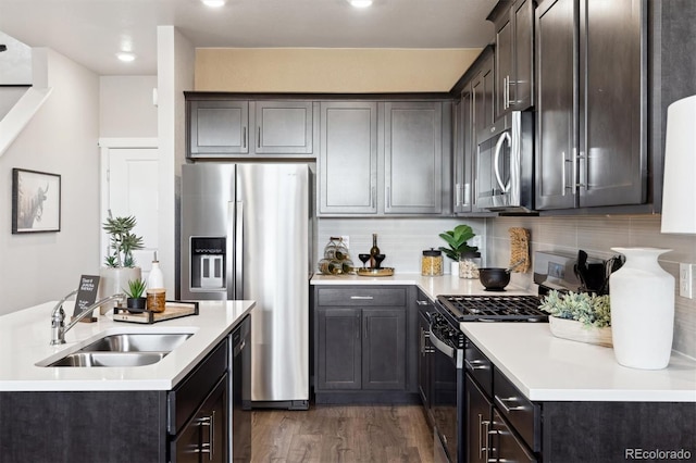 kitchen featuring stainless steel appliances, a sink, light countertops, backsplash, and dark wood-style floors