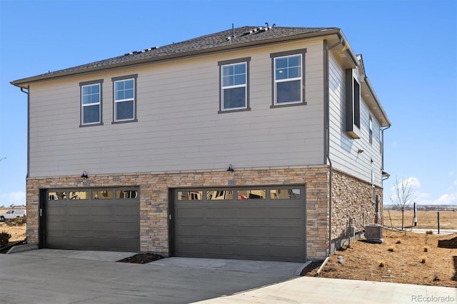 view of side of home with a garage, stone siding, central AC unit, and driveway