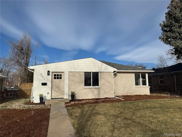 view of front of property with brick siding, a shingled roof, a front yard, and fence