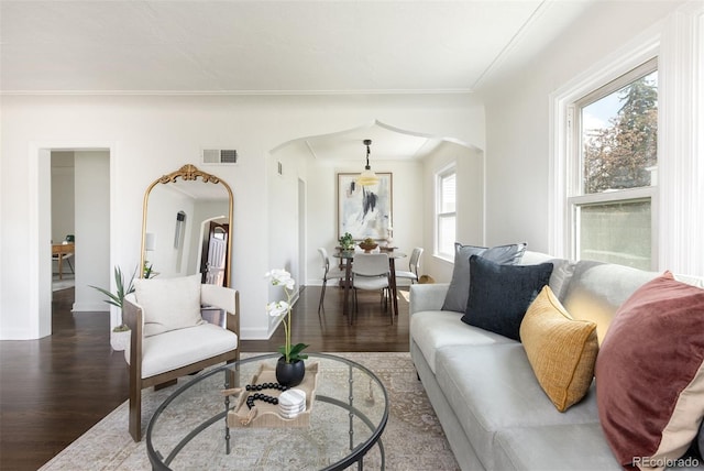living room with arched walkways, wood finished floors, visible vents, and baseboards