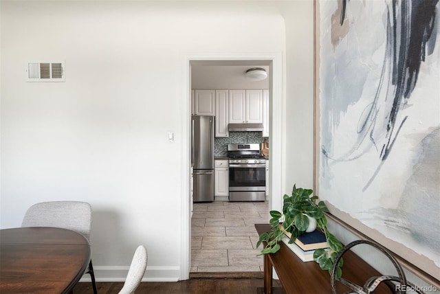 kitchen with wood tiled floor, stainless steel appliances, baseboards, under cabinet range hood, and visible vents