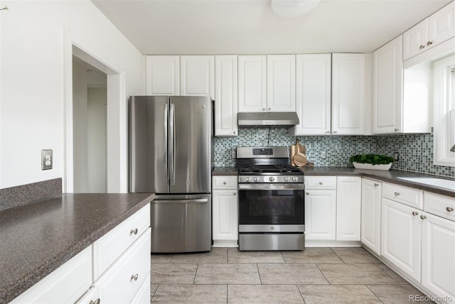 kitchen featuring white cabinets, dark countertops, decorative backsplash, under cabinet range hood, and appliances with stainless steel finishes