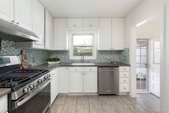 kitchen featuring dark countertops, a sink, appliances with stainless steel finishes, white cabinets, and under cabinet range hood