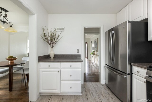 kitchen featuring white cabinets, light wood finished floors, dark countertops, freestanding refrigerator, and visible vents
