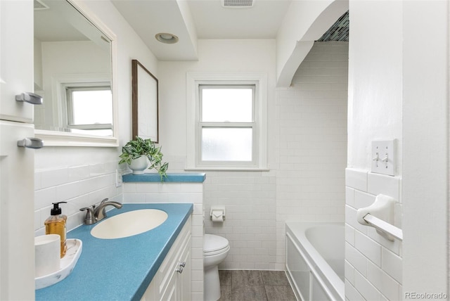bathroom featuring tile walls, a tub, a wealth of natural light, and toilet