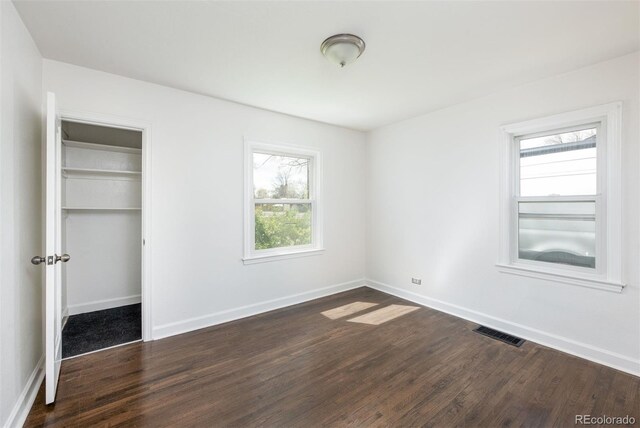unfurnished bedroom featuring baseboards, dark wood-type flooring, visible vents, and a closet