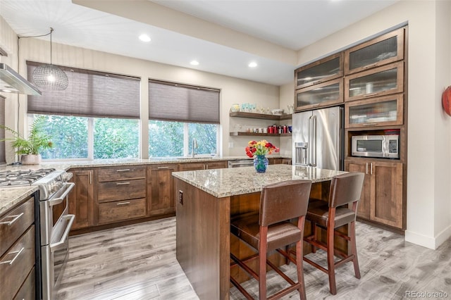 6761 Alan Dr, Denver, CO 80221 - kitchen with stainless steel appliances, a breakfast bar, a center island, light wood-style flooring, and light stone counters