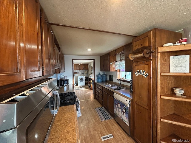 kitchen featuring appliances with stainless steel finishes, washer / clothes dryer, sink, a textured ceiling, and light hardwood / wood-style flooring