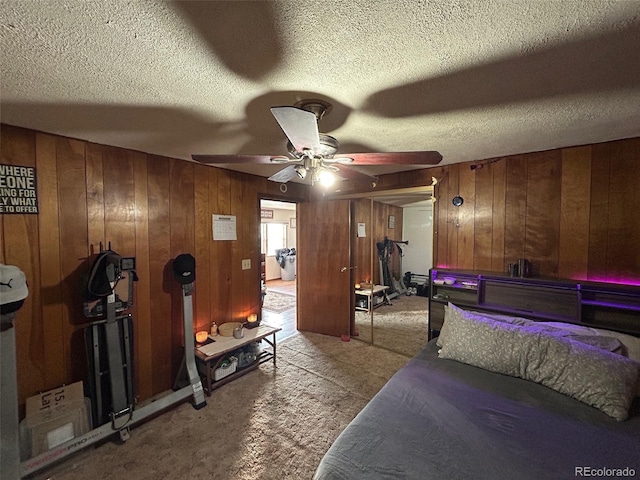 carpeted bedroom featuring ceiling fan, wooden walls, and a textured ceiling