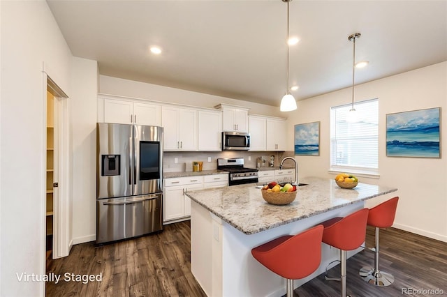 13376 Willow St, Thornton, CO 80602 - kitchen with appliances with stainless steel finishes, white cabinetry, light stone countertops, dark wood finished floors, and a kitchen island with sink
