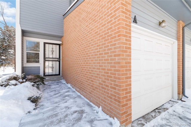 snow covered property entrance featuring a garage and brick siding