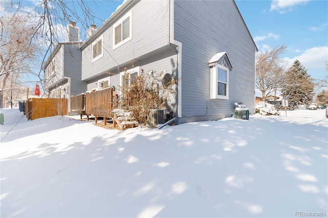 snow covered back of property with cooling unit, fence, and a chimney