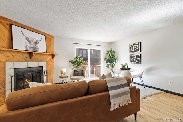 living room featuring a tile fireplace, a textured ceiling, baseboards, and wood finished floors