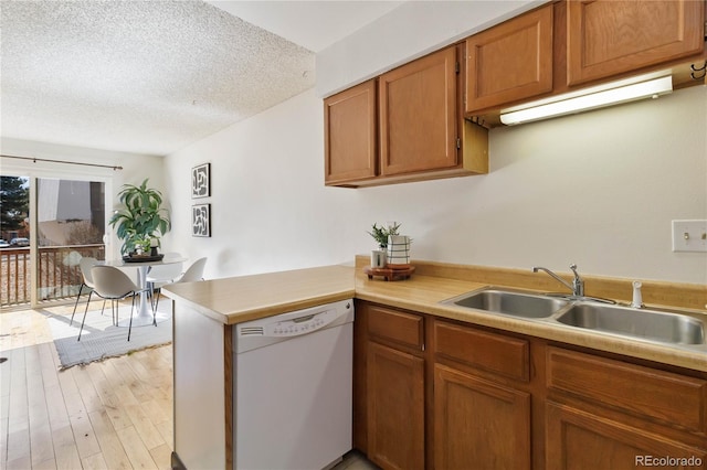 kitchen with a peninsula, white dishwasher, a textured ceiling, light wood-type flooring, and a sink