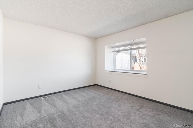 spare room featuring a textured ceiling, carpet floors, visible vents, and baseboards