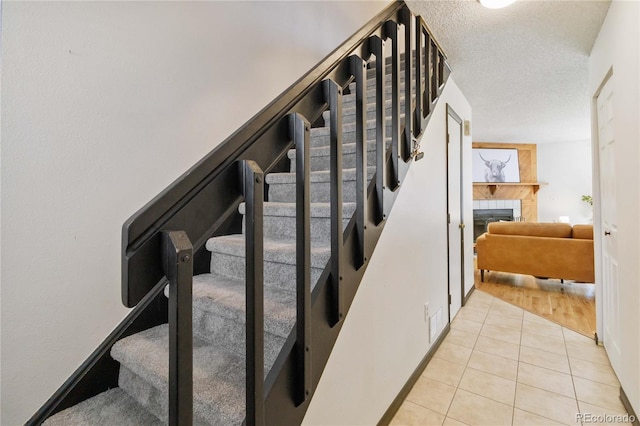 staircase featuring a textured ceiling, a fireplace, and tile patterned floors