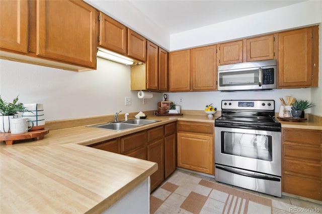 kitchen with brown cabinets, light floors, stainless steel appliances, light countertops, and a sink