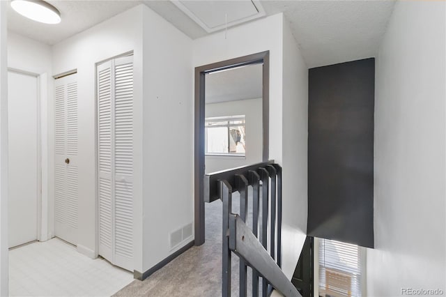 hallway featuring visible vents, attic access, light carpet, a textured ceiling, and an upstairs landing