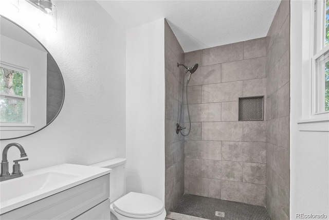 bathroom featuring a wealth of natural light, vanity, tiled shower, and toilet