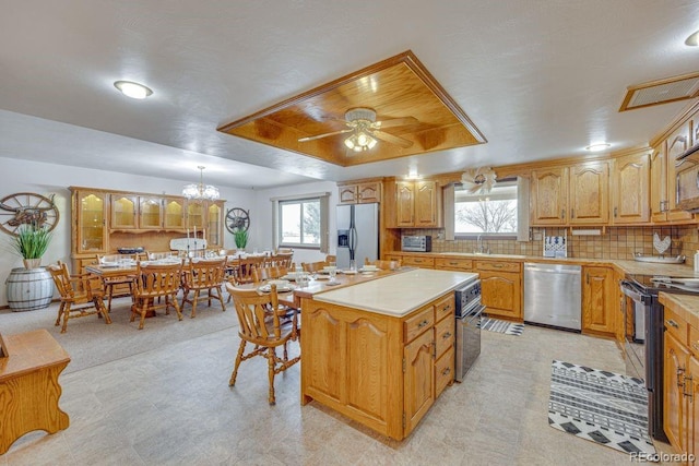 kitchen with hanging light fixtures, stainless steel appliances, a center island, tasteful backsplash, and a raised ceiling