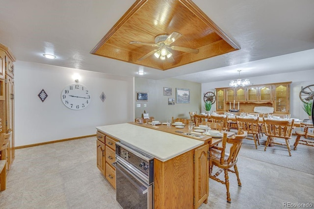 kitchen with pendant lighting, wood ceiling, a tray ceiling, a kitchen island, and ceiling fan with notable chandelier