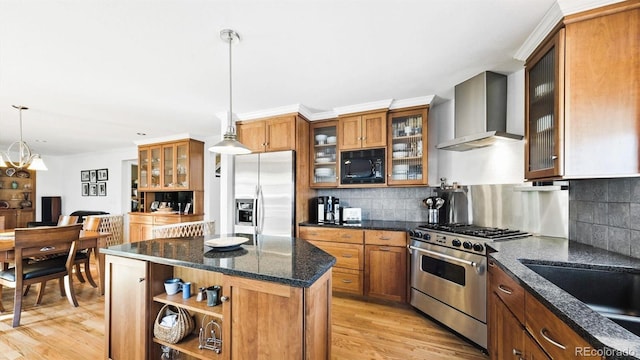 kitchen featuring appliances with stainless steel finishes, a center island, decorative light fixtures, wall chimney exhaust hood, and light wood-type flooring