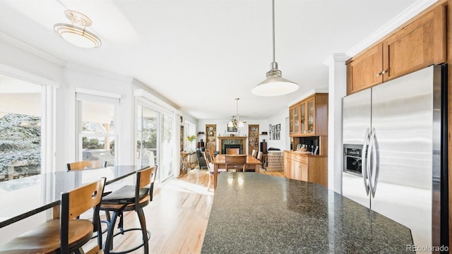 kitchen with stainless steel refrigerator with ice dispenser, a kitchen bar, crown molding, hanging light fixtures, and dark stone countertops