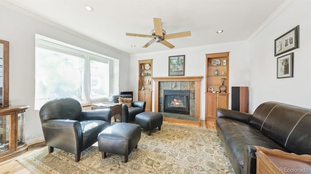 living room featuring built in features, ornamental molding, a tile fireplace, and light wood-type flooring