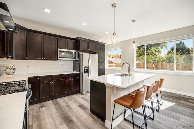 kitchen with sink, stainless steel appliances, backsplash, decorative light fixtures, and a center island with sink