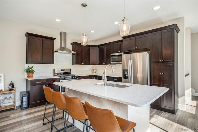 kitchen featuring sink, hanging light fixtures, light hardwood / wood-style flooring, wall chimney exhaust hood, and stainless steel appliances