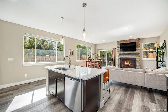 kitchen with sink, hanging light fixtures, stainless steel dishwasher, an island with sink, and a fireplace