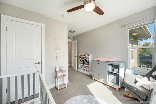 bedroom with ceiling fan, light carpet, and a nursery area