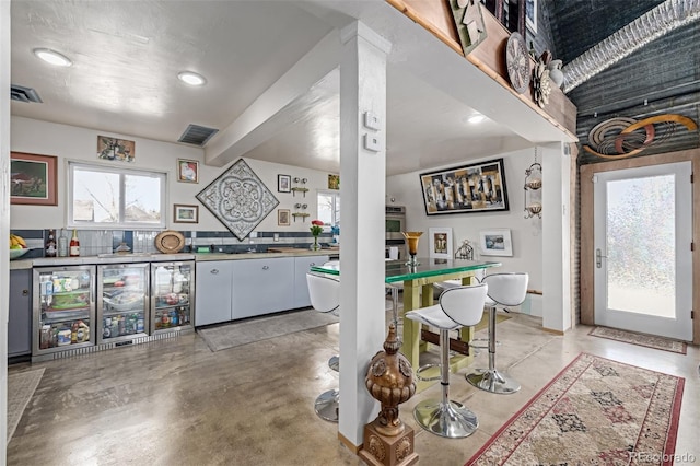 kitchen with beverage cooler, visible vents, white cabinetry, and concrete floors