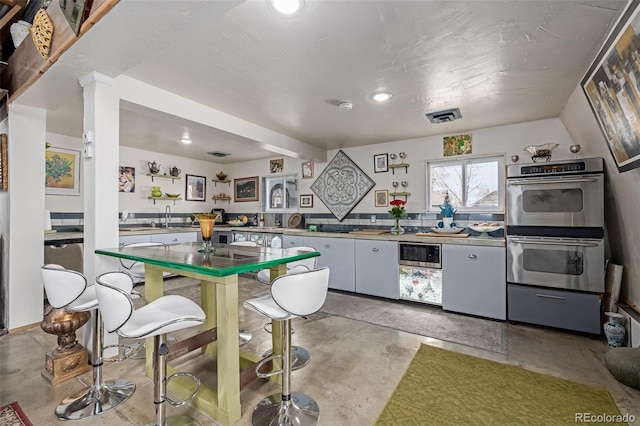 kitchen with stainless steel double oven, concrete floors, visible vents, and a sink