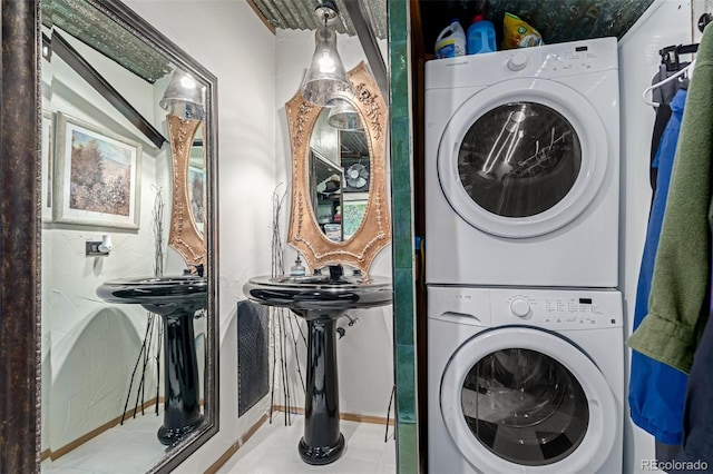 laundry area with tile patterned floors, baseboards, stacked washer and clothes dryer, and laundry area