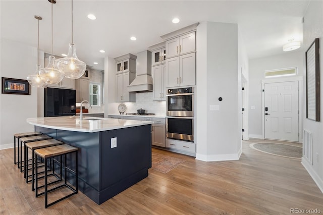 20998 E 60th Pl, Aurora, CO 80019 - kitchen featuring appliances with stainless steel finishes, custom exhaust hood, backsplash, light wood-type flooring, and a breakfast bar area