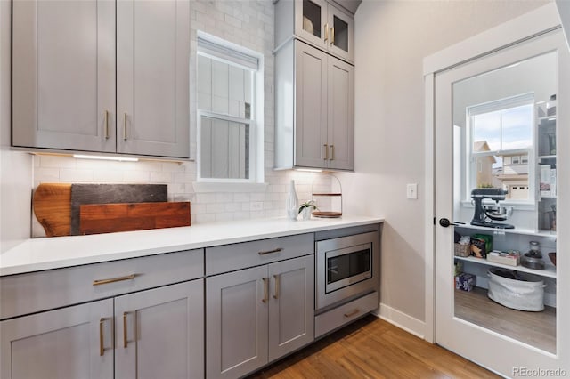 20998 E 60th Pl, Aurora, CO 80019 - kitchen with gray cabinets, stainless steel microwave, light wood-style flooring, and decorative backsplash