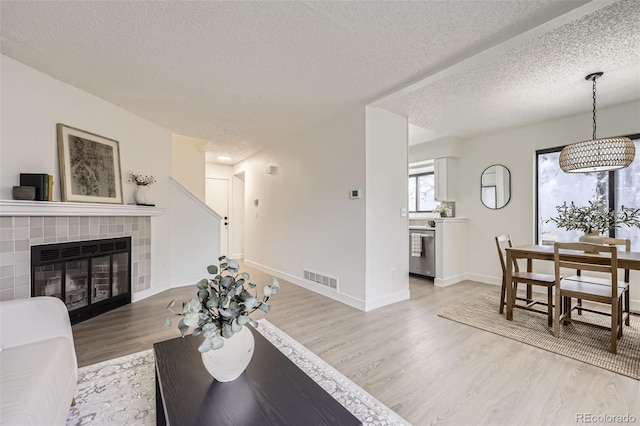 living area featuring visible vents, a tiled fireplace, a textured ceiling, light wood finished floors, and baseboards