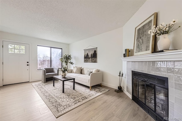 living room featuring baseboards, a fireplace, light wood-type flooring, and a textured ceiling