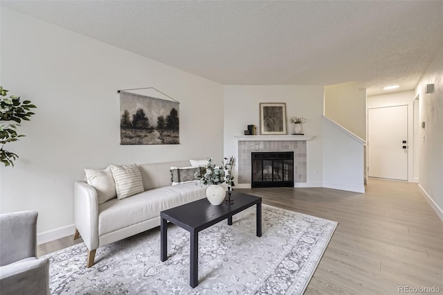 living room featuring baseboards, a textured ceiling, wood finished floors, and a tile fireplace