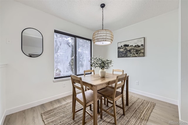 dining area featuring light wood-style flooring, baseboards, and a textured ceiling