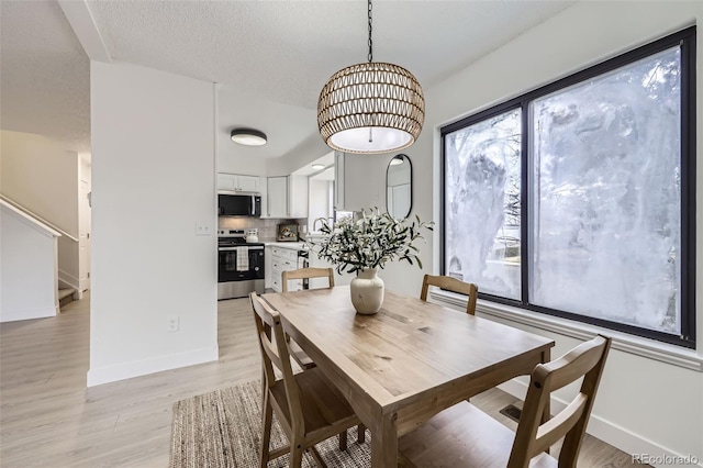 dining room featuring stairway, baseboards, light wood-style floors, and a textured ceiling