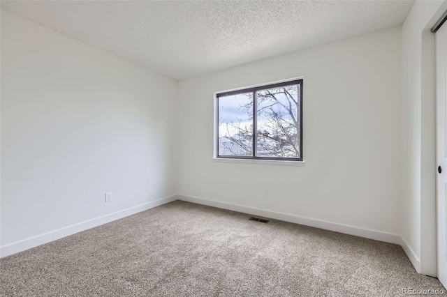 empty room with carpet, baseboards, and a textured ceiling