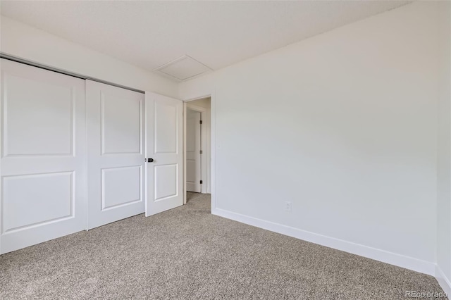 unfurnished bedroom with a closet, baseboards, light colored carpet, and attic access