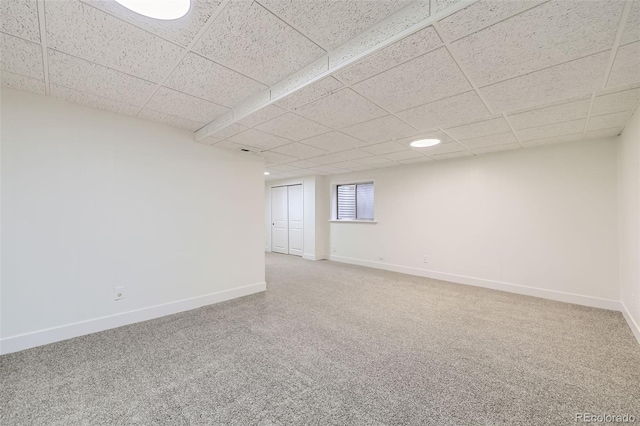 carpeted spare room featuring a drop ceiling and baseboards