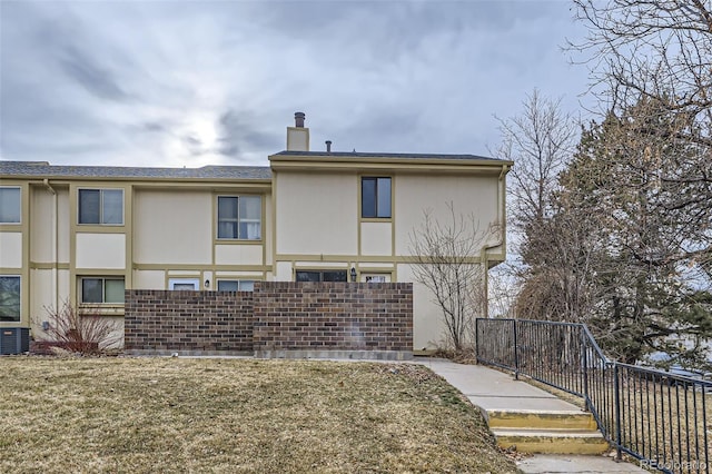 rear view of house featuring stucco siding, a yard, fence, and a chimney