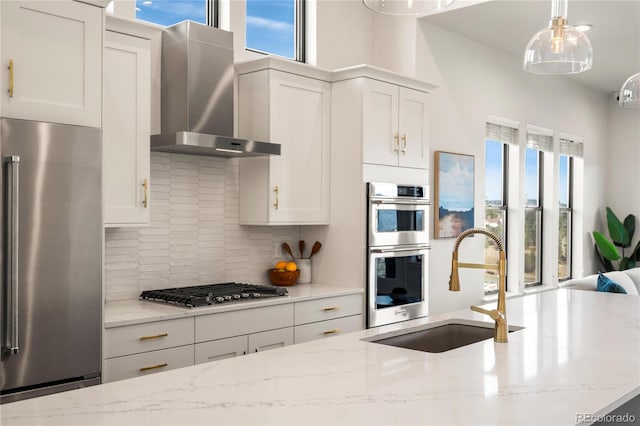 kitchen with light stone countertops, appliances with stainless steel finishes, wall chimney exhaust hood, and plenty of natural light