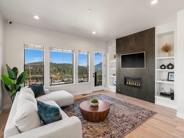 living room with built in features, a tile fireplace, and light hardwood / wood-style flooring