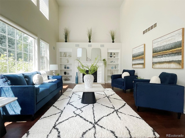 living room featuring dark wood-type flooring, a towering ceiling, and built in features